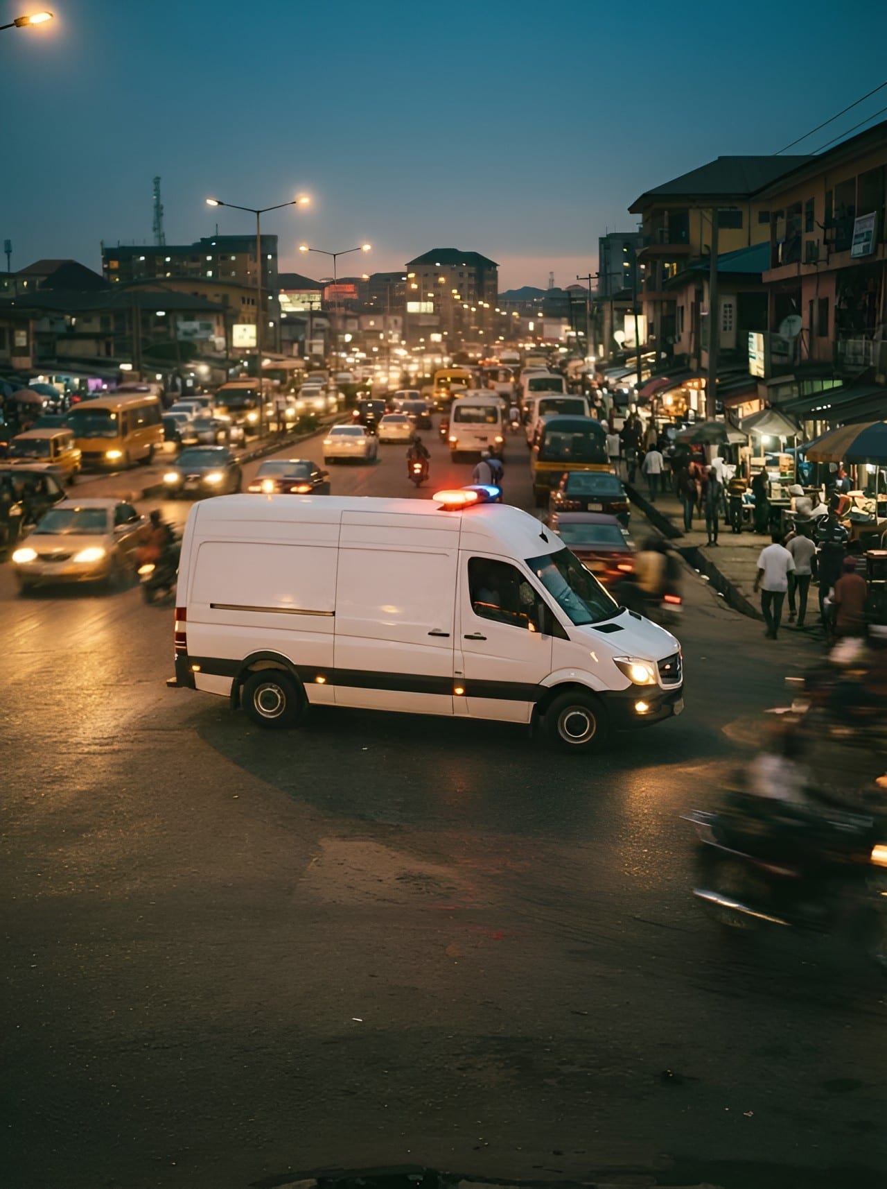 An ambulance with its light bar on driving through city traffic at dusk